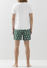 Pánská bílá košile s krátkým rukávem a zelenými plavkami s vzorem, na kterých jsou bílé surfové prkna. Materiál je lehký a má uvolněný střih.