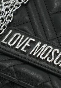 Borsa in pelle nera trapuntata con un'etichetta in argento "LOVE MOSCHINO" e una tracolla a catena, che mette in risalto la sua superficie testurizzata e il design.