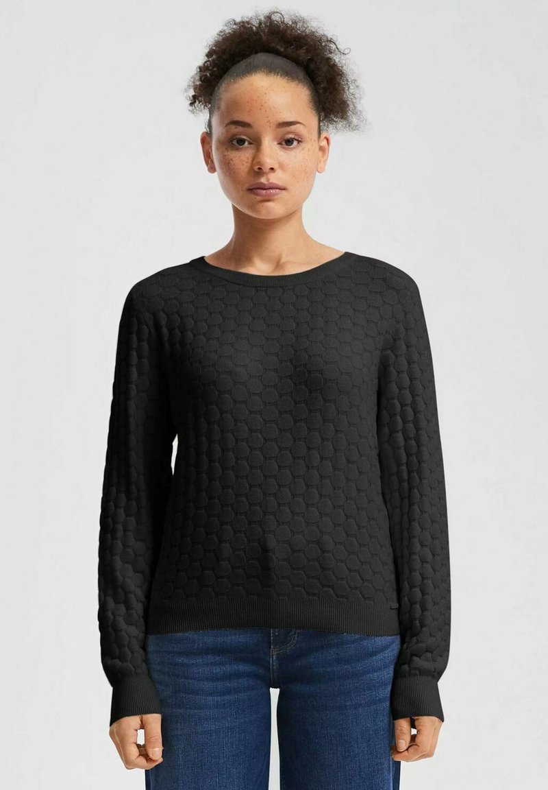 Schwarzer Strickpullover mit Wabenstruktur, langen Ärmeln und rundem Ausschnitt. Kombiniert mit blauen Jeans für einen legeren Look.