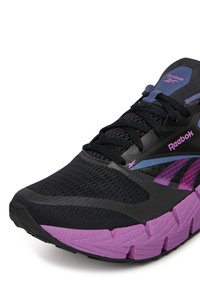 Fekete és lila Reebok futócipő, hálós felsőrésszel, vastag lila talppal és fekete fűzővel, elölről, jobb szögből látható.