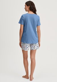 Helles blaues kurzärmliges T-Shirt mit Rundhalsausschnitt, kombiniert mit weißen Shorts, die ein florales Muster in Blau und Grün aufweisen.