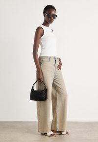 Jeans a gamba larga di colore azzurro chiaro, top senza maniche bianco, borsa nera e sandali bianchi con una texture liscia. Gli occhiali da sole neri completano il look.