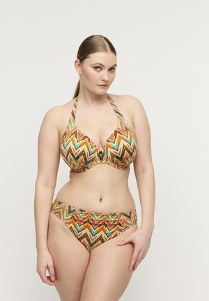 Vrouw in kleurrijke zigzag-bikini met halternek poseren tegen een effen lichte achtergrond.