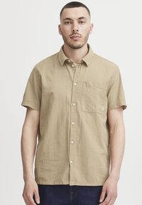 Kortearm, khaki knoopoverhemd van een getextureerde stof met een enkele borstzak en witte knopen, ontworpen voor een relaxte pasvorm.