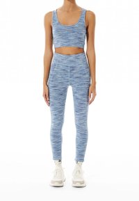 Ljusblå, strukturerad sport-bh och hög midja leggings, båda med en melerad mönster, ihop med vita träningsskor.