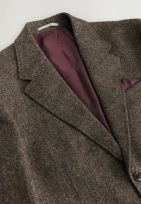 Brown tweed jacket with a textured exterior, a maroon lining, and a pocket square. Features a notched lapel and a single button closure.
