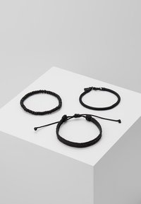 Tre svarte armbånd: ett elastisk perlearmbånd, ett lærvevd med lås, og ett enkelt flettet med justerbar knute.