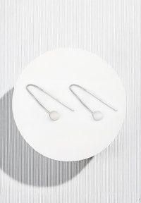 Silvriga örhängen med en lång kedja och en cirkulär skiva. Skivan är slät och matt, med en vriden kedja som ger textur.