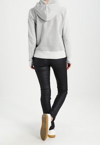 Szara bluza z kapturem z kieszenią kangurką, zestawiona z dopasowanymi czarnymi dżinsami i białymi trampkami z beżową podeszwą.