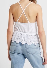 Vit bomullstopp med korskorsade axelremmar och en samlad ögla spets nertill. Kombinerad med ljusblå jeans med hjärtformade fickor.