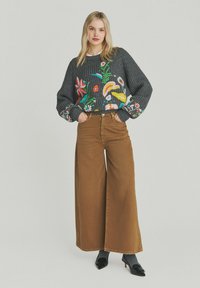 Grå strikket trøje med farverig blomsterbroderi, kombineret med brune vidde ben bukser. Tekstureret stof og afslappet pasform. Sorte hæle fremhæver outfittet.