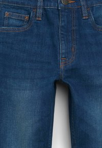 Jeans de mezclilla azul oscuro con costuras naranjas, diseño slim fit, pequeño bolsillo frontal y cierre de botón clásico en la cintura.