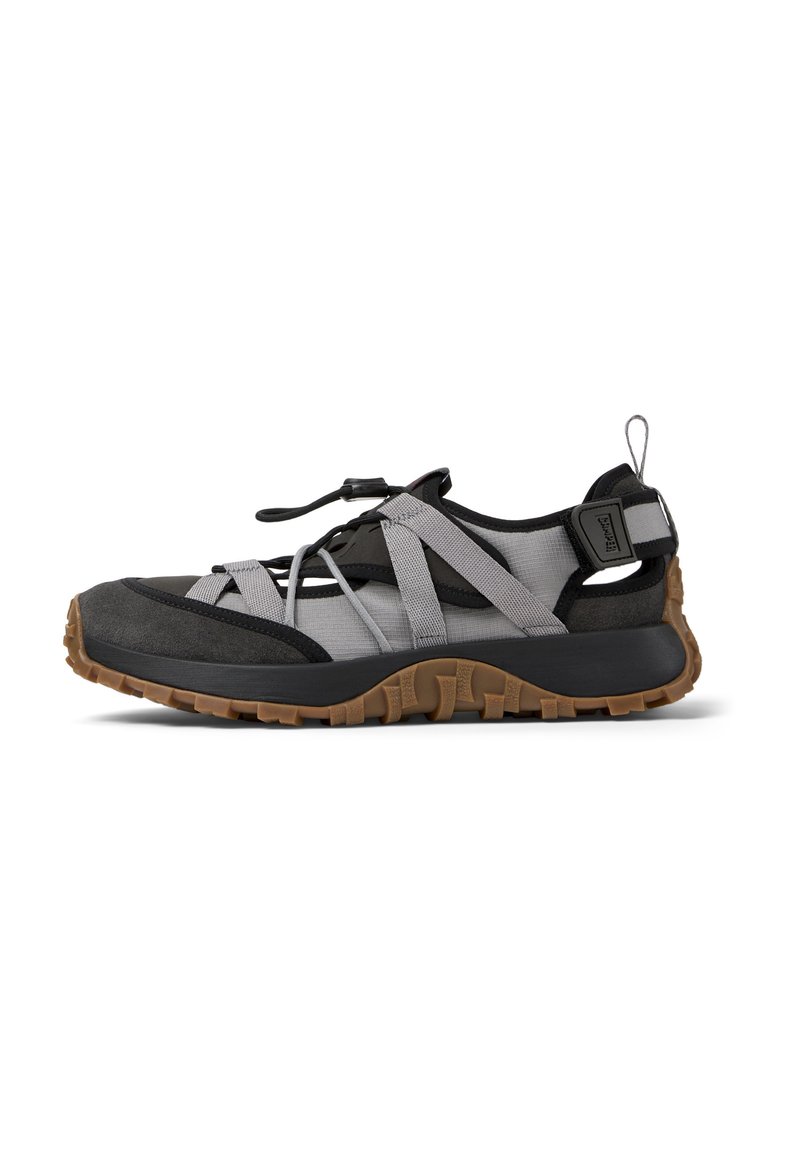 Scarpa sportiva con tomaia in tessuto nero e grigio, suola in gomma, strappi elastici e un'etichetta per facilitarne l'indossamento. Presenta una suola esterna con grip testurizzato.