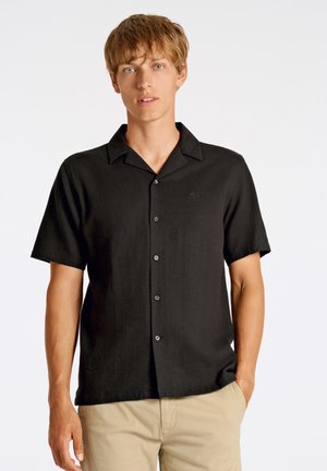 Chemise noire à manches courtes, boutonnée, en tissu léger avec un col décontracté, présentant un logo discret et des boutons gris.