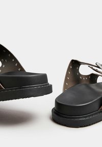 Sandali platform neri con una fascetta testurizzata decorata da borchie argentate, suola spessa e opaca, e punta arrotondata.