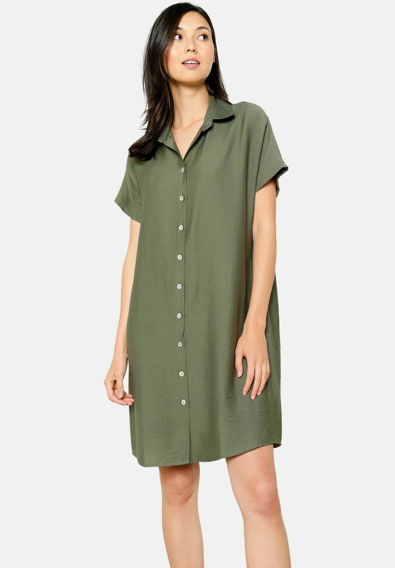 Abito camicia corto a maniche corte verde oliva realizzato in tessuto morbido, con chiusura a bottoni davanti, colletto e vestibilità ampia.