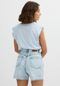 Camisa de algodón azul claro con mangas tipo cap sleeve, combinada con pantalones cortos de mezclilla de tiro alto en un lavado claro, que presentan un dobladillo deshilachado y bolsillos traseros.