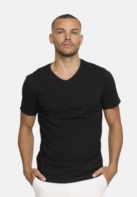 T-shirt noir à manches courtes et décolleté en V, fabriqué en tissu coton à la texture lisse, au design ajusté et avec un minimum de détails de couture.