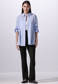 Camicia button-up azzurro chiaro, maniche lunghe arrotolate, abbinata a pantaloni neri a zampa d'elefante e ballerine nere con decorazioni. Design semplice e strutturato.