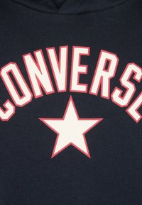 Námořnická mikina s velkým textem "CONVERSE" v bílé barvě s červeným obrysem a centrální bílou hvězdou. Měkká, texturovaná látka s pohodlným střihem.