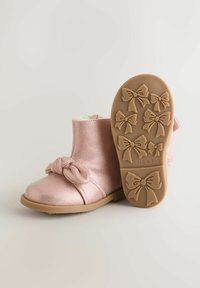 Botine metalizate roz, cu un detaliu sub formă de fundă în față, căptușeală texturată din pluș și o talpă din cauciuc maro, având model de funde.