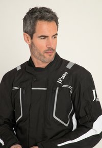 Czarna kurtka z tkaniny z szarymi akcentami, z wieloma kieszeniami na zamek z przodu, podniesionym kołnierzem i logo na ramieniu.