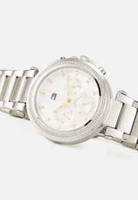 Montre en acier inoxydable argenté avec un cadran rond blanc, accents dorés, lunette en cristal et un design de chronographe à trois sous-cadrans.