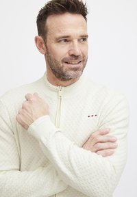 Cremefarvet lynlånsweater med et struktureret mønster, ribbede manchetter og en lille logoaccent. Blødt stof med en tætsiddende pasform.