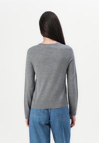Gray knit sweater with long sleeves, round neckline, and ribbed hem. Worn with high-waisted blue denim jeans, showing a smooth texture.