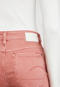Närbild av en person som bär rosa denimjeans och en vit ribbad långärmad topp, där bakfickan och midjeområdet visas.
