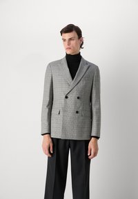 Grå rutig dubbelknäppt blazer med svarta knappar, skräddarsydd passform, snedskurna slag, strukturerad tyg, bärs över en svart polo.