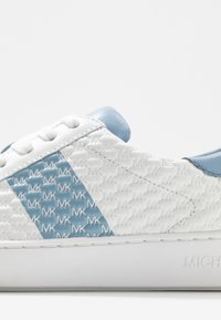 Biała tenisówka z fakturowanym wzorem, z jasnoniebieskim akcentem i logo. Gładka, niebieska część na pięcie dopełnia design.