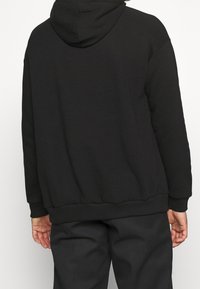 Černá mikina s kapucí a pohodlným střihem, s ribkovanými manžetami a lemem. Vyrobena z měkké tkaniny a zdobí ji jednoduchý, minimalistický design.