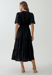 Black, tiered midi dress with a relaxed fit, short puff sleeves, and a cinched waist. Made of lightweight, textured fabric.