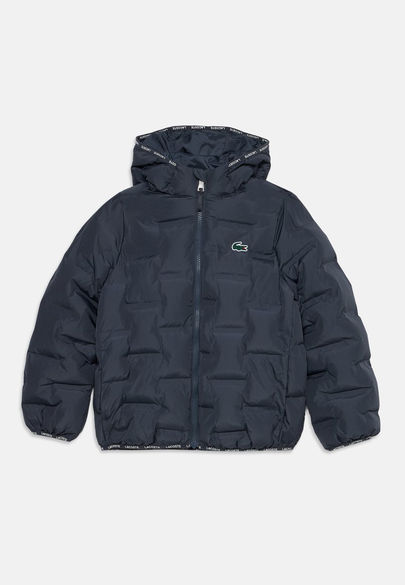 Veste matelassée bleu foncé avec capuche, fermeture éclair intégrale devant, bordure de texte Lacoste et logo crocodile vert sur la poitrine.