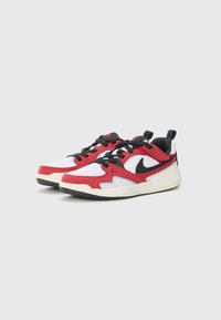 Sneaker rosse e bianche con tomaia in rete, dettagli neri e suola testurizzata. Il design presenta un logo ben visibile e un motivo a zigzag.