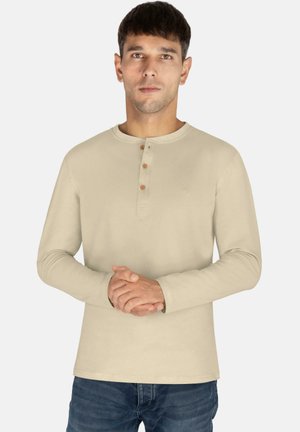Helles beige Langarmhemd mit rundem Ausschnitt, drei Holzknöpfen und einem dezenten Logo auf der Brust. Hat eine glatte Textur.