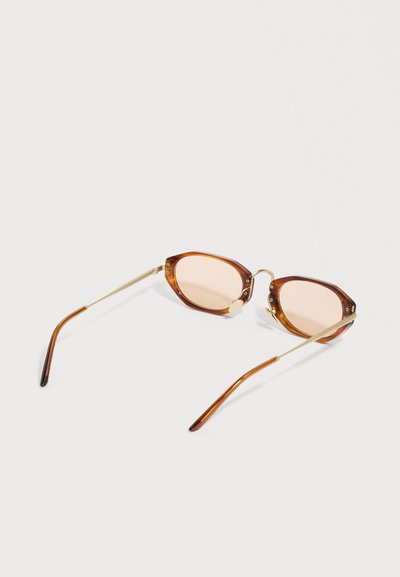 Οβάλ γυαλιά ηλίου με ταρταρούγα πλαίσιο, χρυσαφένιους μεταλλικούς βραχίονες και φακούς με ανοιχτό καφέ απόχρωση, τοποθετημένα πάνω σε λευκή επιφάνεια.