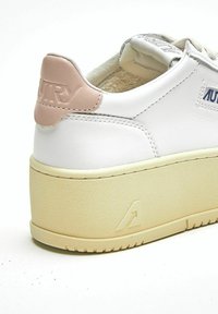 Sneaker in pelle bianca con tallone rosa chiaro, suola in gomma beige, dettagli strutturati e logo del marchio in rilievo sul tallone.