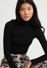 Sort langærmet turtleneck-top lavet af et glat, strækbart stof, tætsiddende design, båret med blomsterprint højtaljede bukser.