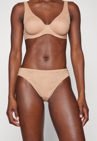 Soutien-gorge en dentelle nue et culotte assortie avec un motif floral texturé, tissu doux, bretelles larges et design sans couture, offrant confort et soutien.