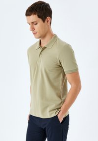 Camisa polo caqui con un cuello texturizado y mangas cortas, que presenta un corte clásico y una tela suave. Combinada con pantalones navy.