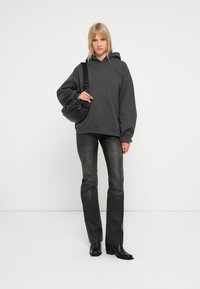 Haut gris foncé surdimensionné en tissu doux, associé à un jean noir et des bottes à talons noires. Portant un petit sac à main noir froncé.