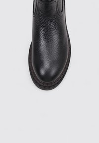 Bottine en cuir noir avec une surface texturée, bout rond et semelle brune contrastante. Détails cousus le long des bords.