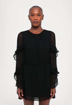 Vestido negro con mangas largas transparentes y con volantes, cuello redondo y cierre con lazo en el cuello. Tejido fluido con un corte holgado.
