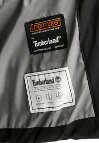 Étiquettes en tissu noir sur une doublure intérieure grise : "Thermore pour Timberland" et "Timberland Crafted Since 1973" avec des icônes d'isolation et d'entretien.