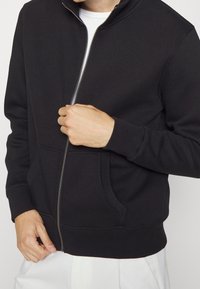 Svart zip-up sweatshirts med hög krage, sidofickor, ribbade ärmslut och nederkant, tillverkad av mjukt, texturerat tyg.