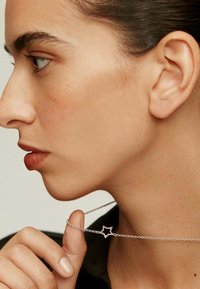 Collar con colgante en forma de estrella plateada sobre una cadena delicada, sostenido por una mano, contra un fondo neutro con enfoque en los detalles de la joyería.
