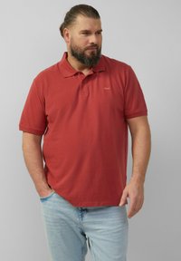 Bordowa koszula polo z klasycznym kołnierzykiem, krótkimi r�ękawami i małym logo na piersi. Połączona z jasnoniebieskimi dżinsami.