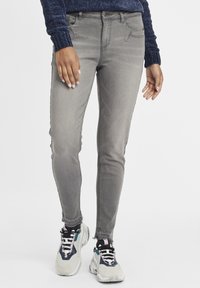 Jeans skinny de denim gris con una textura suave, dos bolsillos frontales y un diseño de tiro medio, combinados con zapatillas gruesas que presentan acentos multicolores.